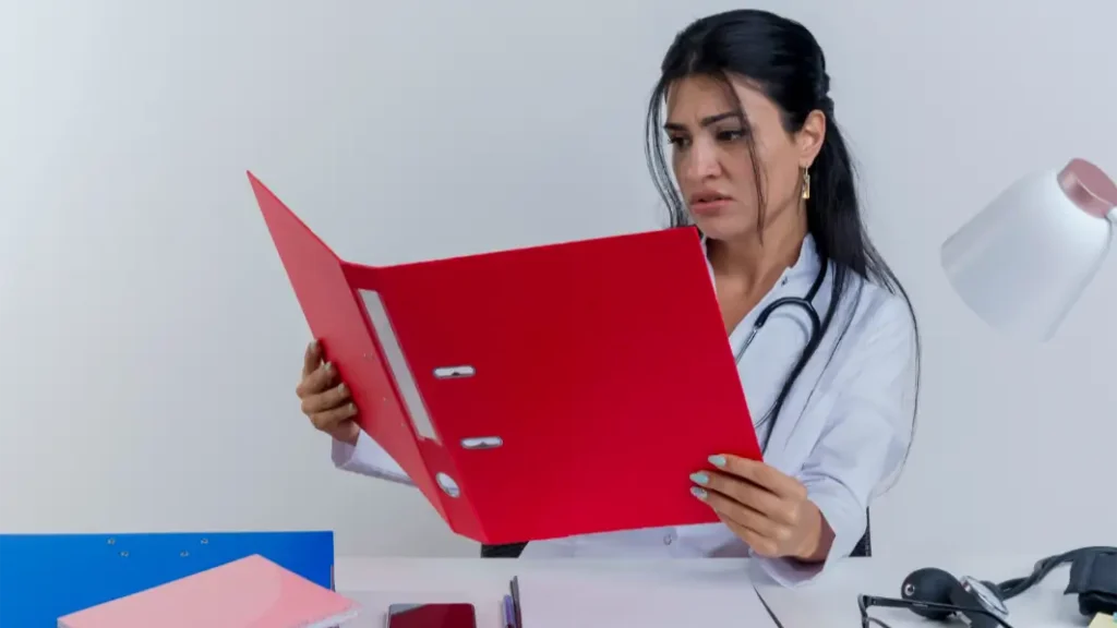 Doctora con gesto preocupado revisando un expediente médico en su escritorio